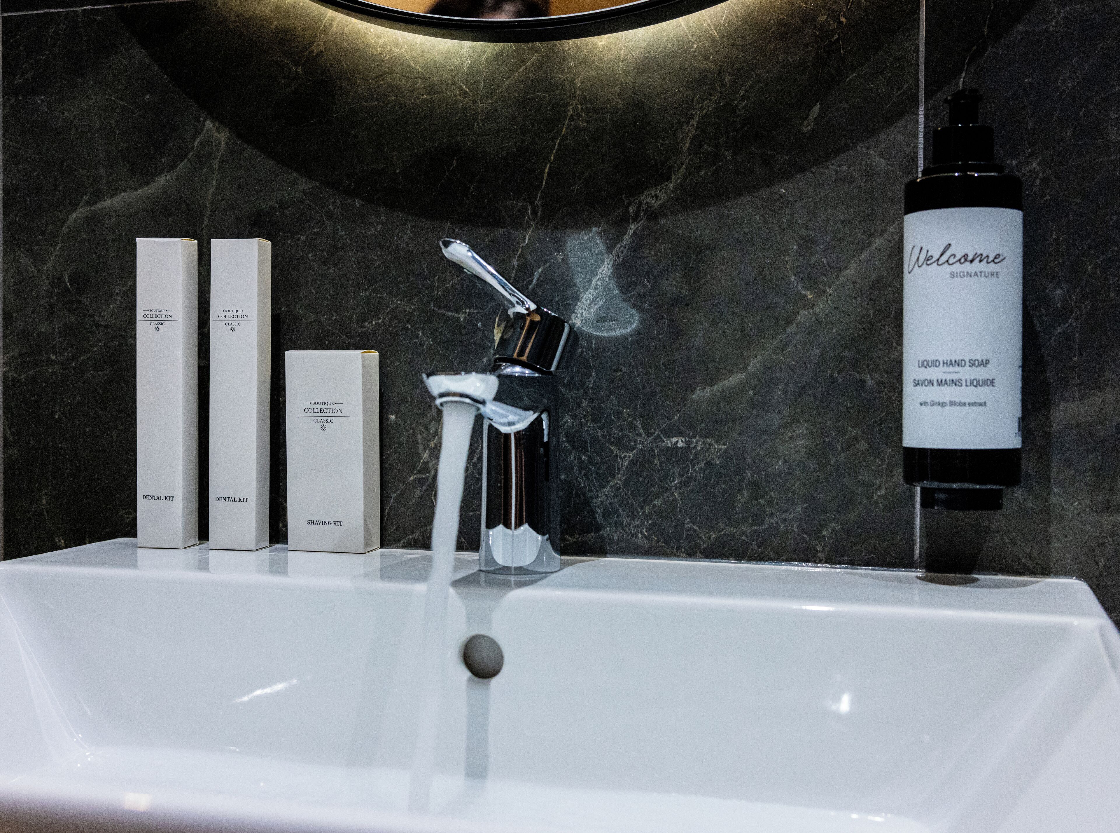 Une salle de bain avec un lavabo en marbre, un robinet et deux boîtes étiquetées « Trousse de soins dentaires » et « Trousse de rasage ».