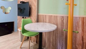 Una stanza con un tavolo rotondo, una sedia verde, un ritaglio di Topolino attaccato al muro e una decorazione alta a forma di matita.