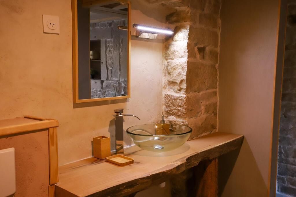 Une salle de bain avec un mur en pierre, un lavabo en forme de bol en verre, un meuble-lavabo en bois et un miroir.
