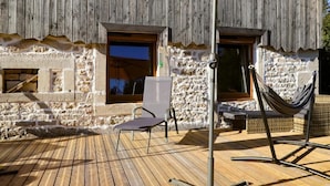 Une terrasse en bois avec un hamac et une chaise, un mur en pierre et une fenêtre.