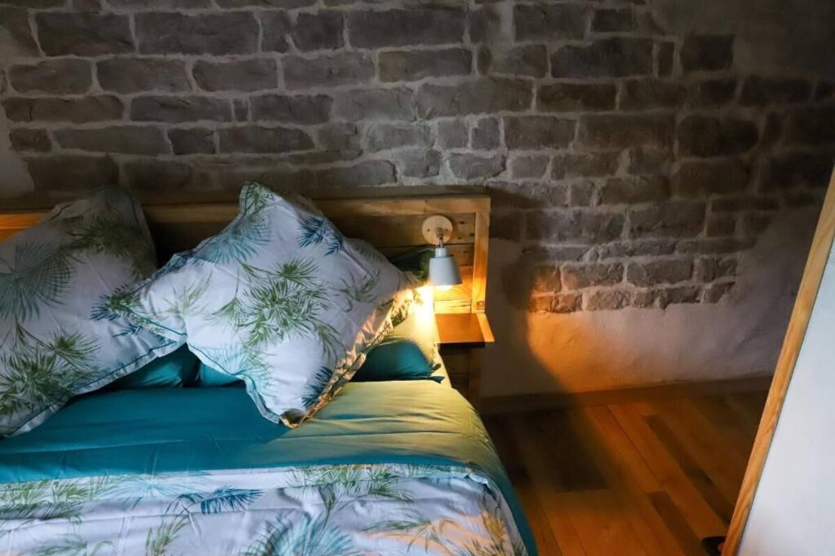 Een gezellige slaapkamer met een stenen muur, een houten hoofdbord en een bedlampje.