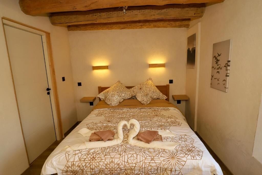 Un dormitorio con una cama grande, dos luces fijadas a la pared, techo de madera y una puerta.