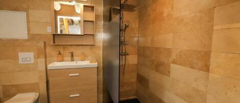 Een badkamer met een houten wastafelmeubel, een spiegel, een toilet en een douchehoek.