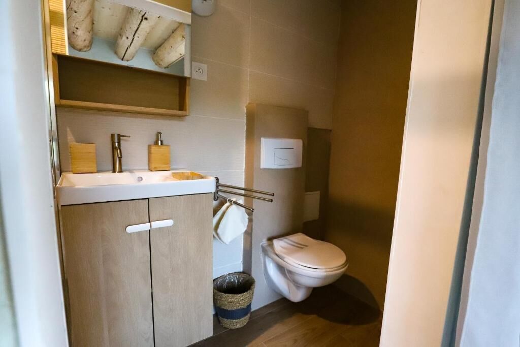 A compact bathroom with a wooden cabinet, a sink, a toilet, and a trash bin.