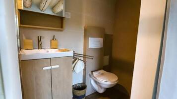 A compact bathroom with a wooden cabinet, a sink, a toilet, and a trash bin.
