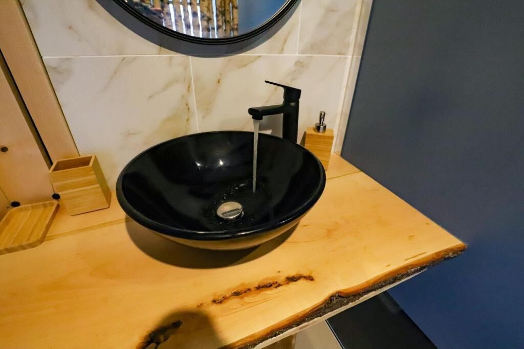 Un vasque noir, encastré dans un plan de travail en bois, avec un pare-éclaboussures en marbre et un miroir au-dessus.