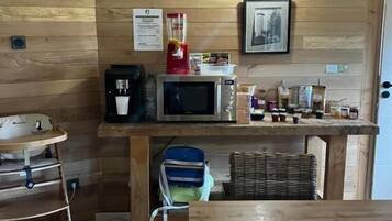 Een compacte keuken met houten wanden, een magnetron, een koffiezetapparaat en diverse etenswaren op het aanrecht.