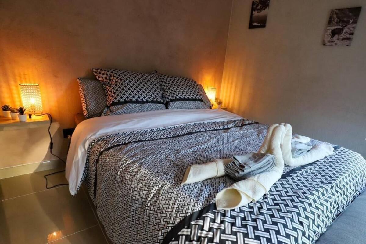 Een net opgemaakt bed met beddengoed met een patroon, een bedlampje en een aan de muur hangend schilderij.