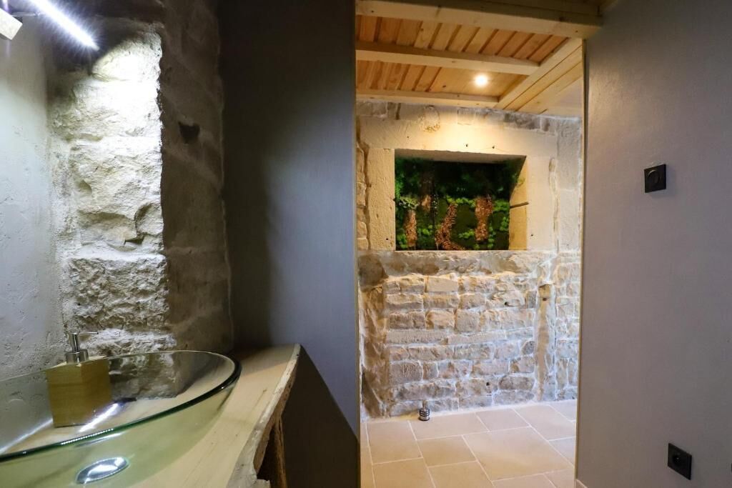 Ein Badezimmer mit einem Glaskonstruktion-Waschbecken, Steinwänden und einer Holzbalkendecke.