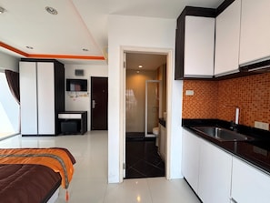 A compact hotel room with a bed, a small desk, a kitchenette, and a bathroom. - Bright Corner Pool-view Studio With Balcony - New Nordic VIP 3, Pratumnak (Pattaya)