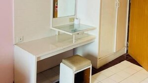 A small, compact room with a white vanity, a mirror, a small stool, and a wardrobe. - Indra Hotel Hatyai (Hat Yai)