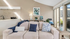 Een moderne woonkamer met een beige bank, een salontafel en een keuken met een spoelbak en aanrecht.