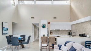 Een moderne woonkamer met een bank, eettafel en stoelen. Er is een keuken met kastjes en een spoelbak.