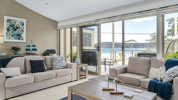 Een moderne woonkamer met twee banken, een salontafel en een grote schuifglazen deur die leidt naar een balkon met uitzicht op zee.