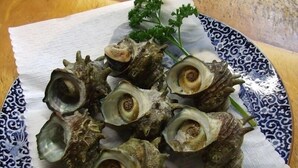 Un plato de caracoles sobre un plato de cerámica con diseño, con un mantelino blanco debajo.