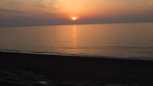 Atardecer sobre un mar tranquilo con una playa en primer plano.