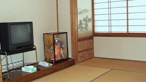 Una habitación tradicional japonesa con suelo de tatami, un televisor sobre un soporte, un cuadro enmarcado y un shoji con una pintura.