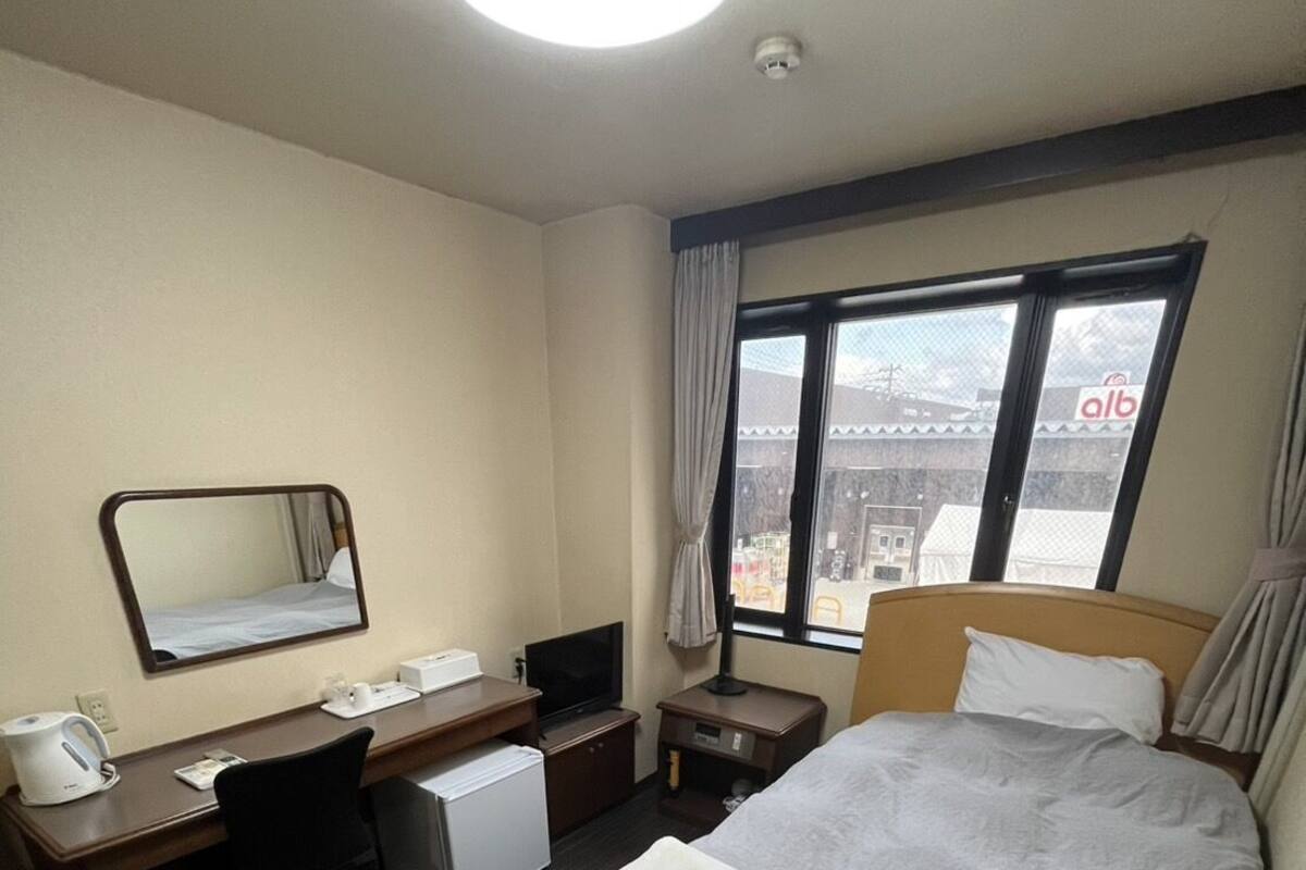 A hotel room with a bed, a desk, a chair, a television, a window with curtains, and a ceiling light.