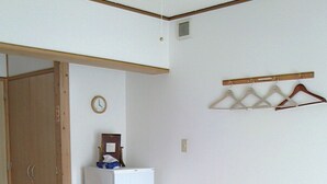 Une pièce avec un plancher en bois, un réfrigérateur blanc, une porte en bois et un porte-vêtements fixé au mur.