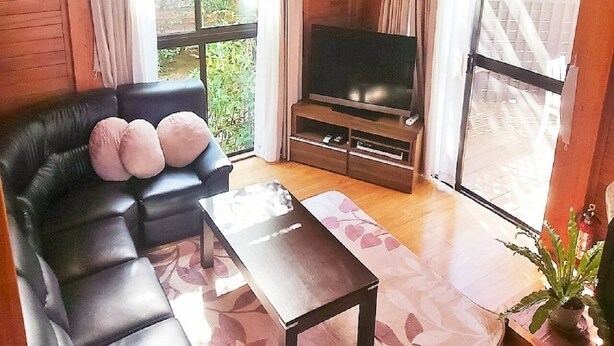 A living room with a black leather sofa, a flat-screen TV, a wooden coffee table, and a large window with curtains. - Cottage Forest Paradiso (Onna)