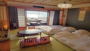 A hotel room with tatami mats, a futon bed, a low table with chairs, and a view of the city through large windows. - Sumie Chita (Minamichita)