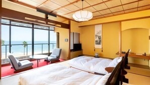 A hotel room with a large bed, a TV, a small table, two chairs, a balcony with a view of the sea, and a traditional Japanese decor. - Sumie Chita (Minamichita)