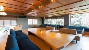 A modern interior with a long wooden table, blue sofas, and large windows providing natural light. - Sumie Chita (Minamichita)