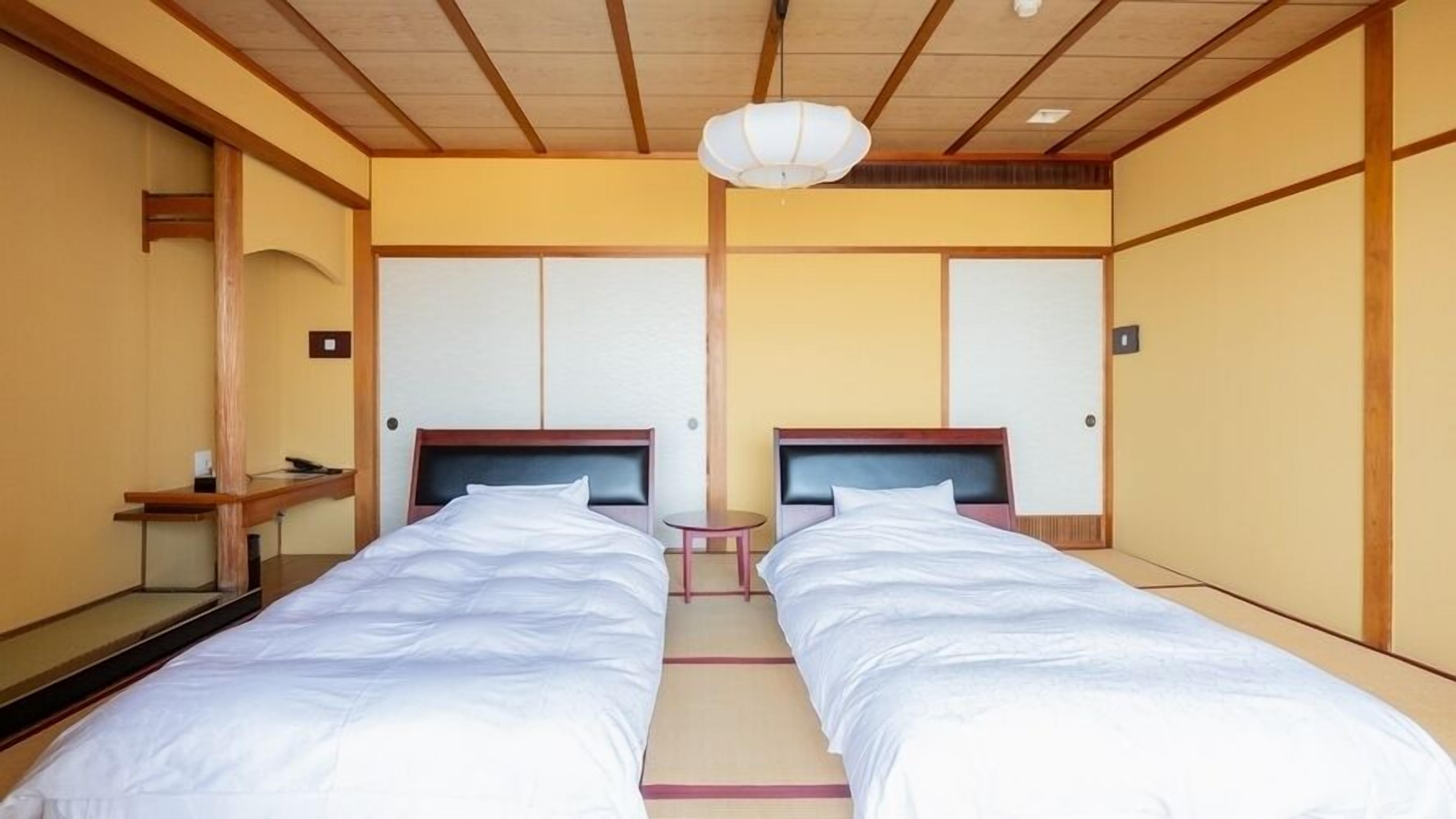 A hotel room with two single beds, a small bedside table, a mirror, and a ceiling light fixture.