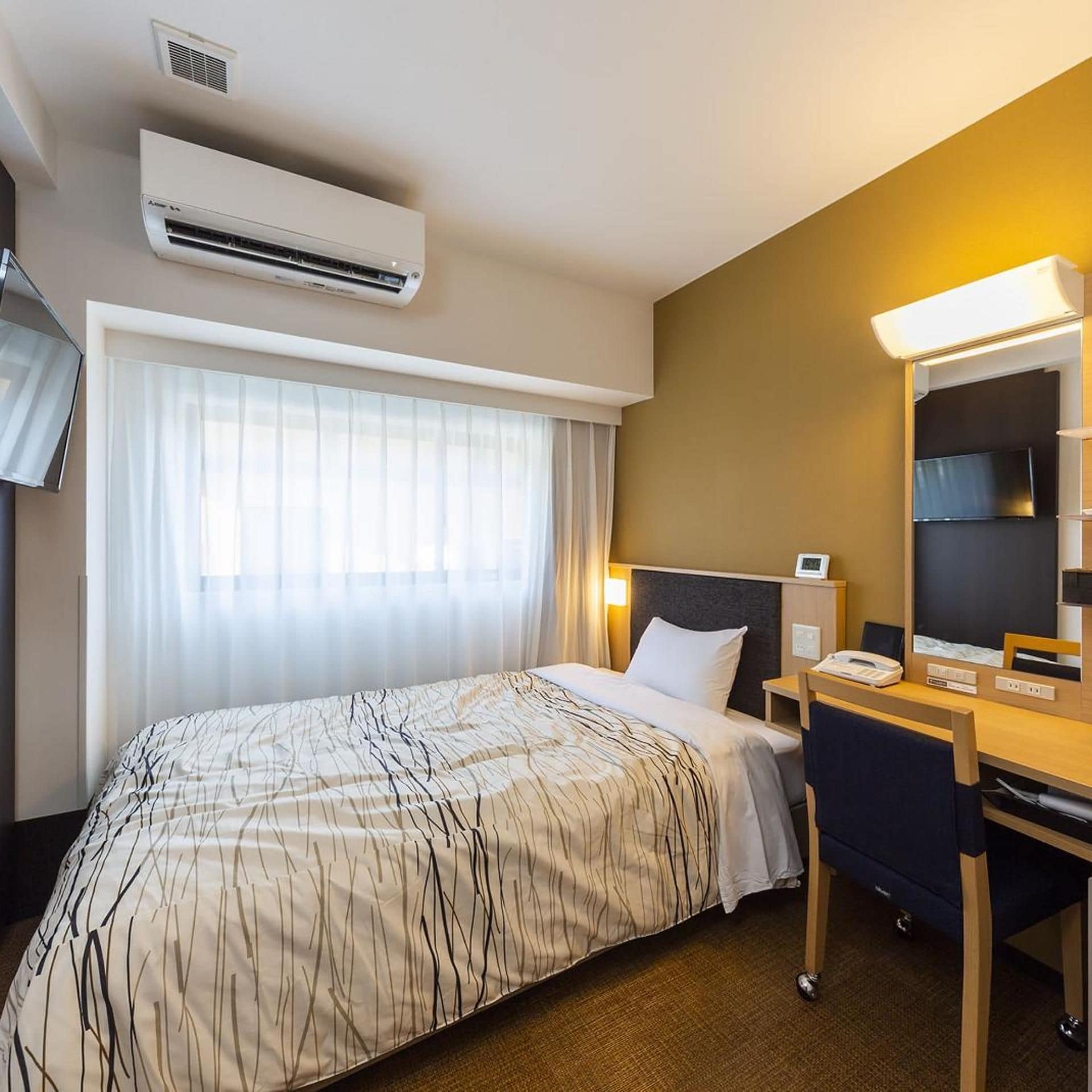 Habitación de hotel con una cama, un escritorio, una silla, una lámpara de escritorio, un televisor de pantalla plana y un aire acondicionado.