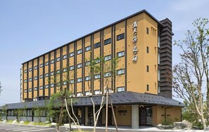 Un hotel de varios pisos con fachada amarilla, un acceso cubierto y cielo despejado.