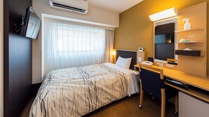 Een hotelkamer met een bed, bureau, stoel en een aan de muur bevestigde televisie.