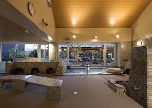 A modern spa area with a stone bench, a stone wall, and a view of an outdoor garden. - Manten no Yu Michi no Yado (Hakusan)