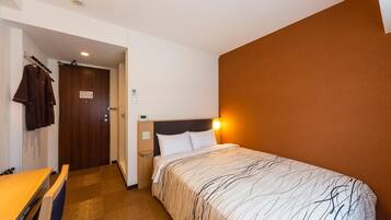 A hotel room with a bed, bedside table, and a desk with chairs.
