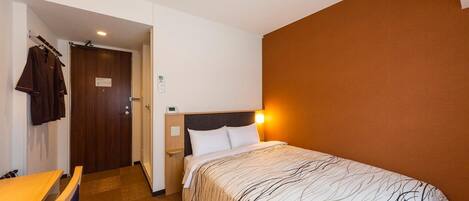 A hotel room with a bed, bedside table, and a desk with chairs.
