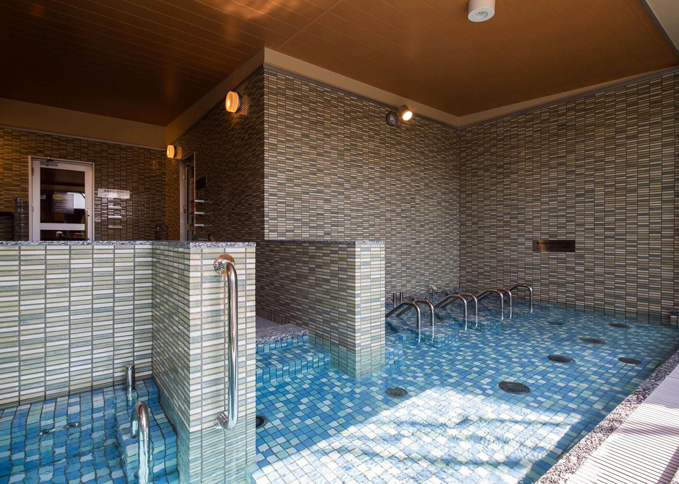 Une piscine intérieure moderne, dotée d’un sol et de murs carrelés, de rampes métalliques et d’un système d’évacuation des eaux claires.