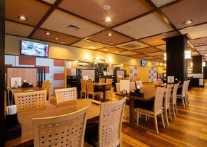 Un restaurant avec plusieurs tables et chaises, un comptoir où est affiché le menu, et un téléviseur fixé au mur.