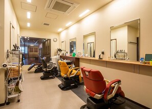 Un salon de coiffure doté de plusieurs fauteuils, de miroirs et d’un comptoir où sont rangés divers outils de coiffure.