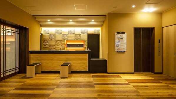 Un espace d’accueil comprenant un comptoir de réception en bois, un panneau d’affichage et un ascenseur.
