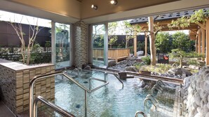 A traditional Japanese onsen with a wooden deck, stone walls, and a view of the surrounding garden. - Manten no Yu Michi no Yado (Hakusan)