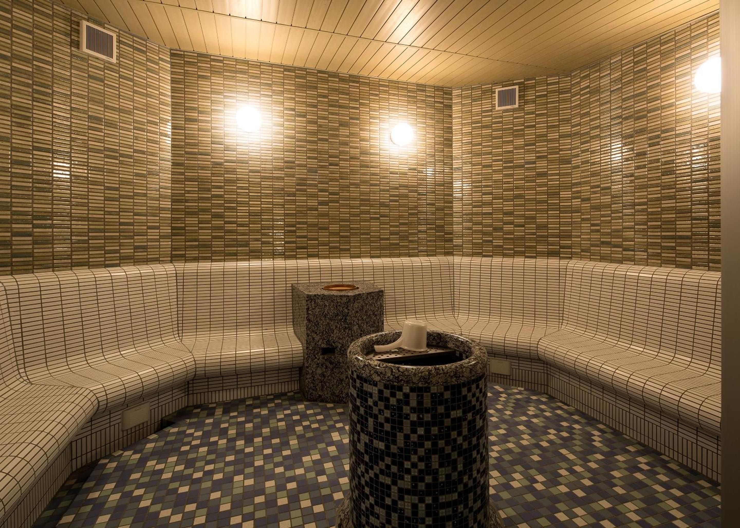 A sauna room with tiled walls and floor, a bench, and a central stone structure.
