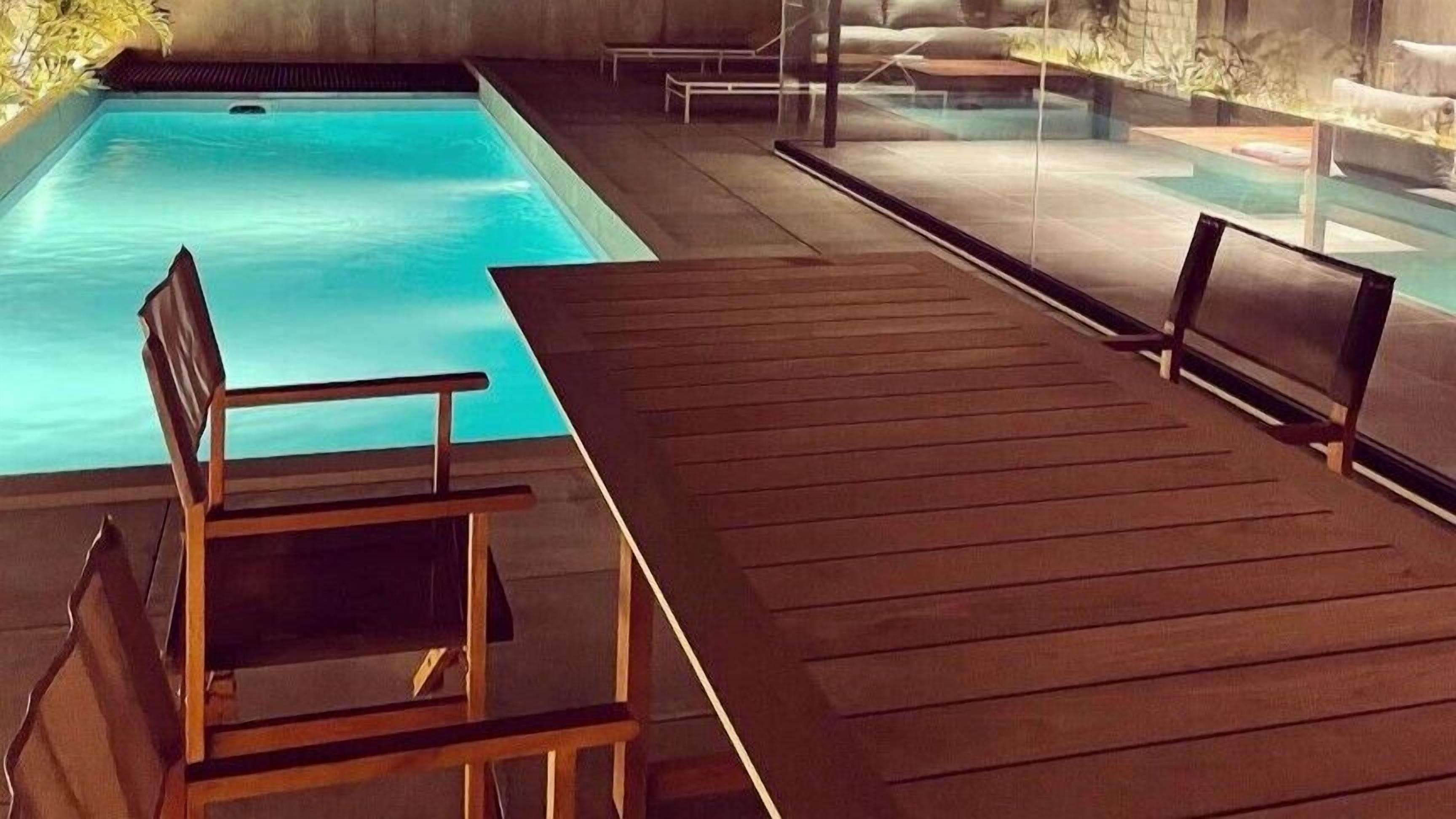 A pool area with a wooden deck, a chair, and a glass barrier.