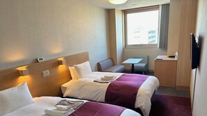 Une chambre d’hôtel avec deux lits, un petit bureau, une chaise et un téléviseur.