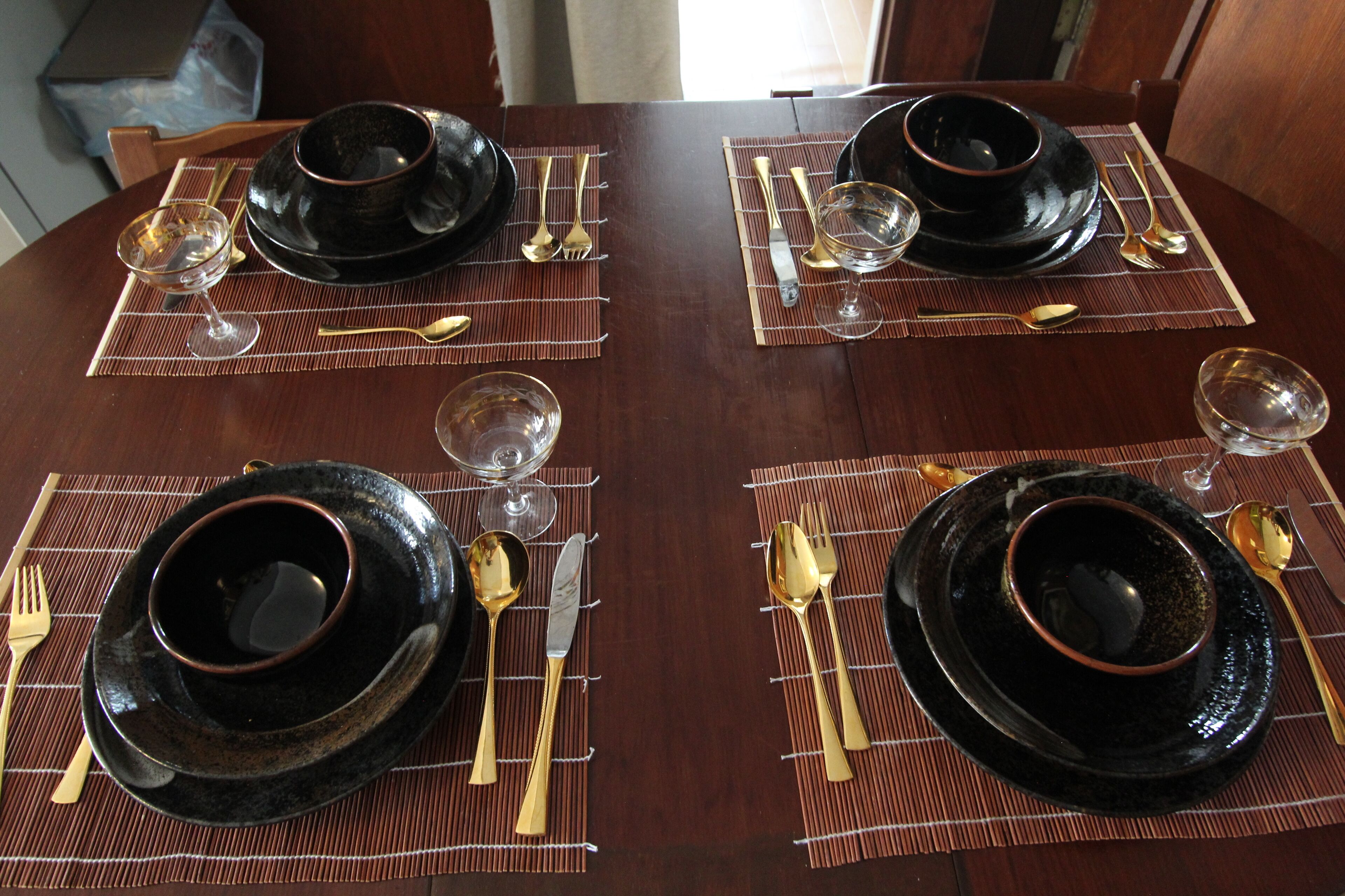 A dining table set with black plates, gold cutlery, and clear wine glasses.