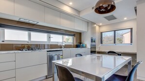 Una cocina moderna con una isla central, electrodomésticos integrados y un comedor con mesa y sillas de vidrio.