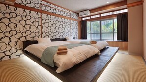 Un dormitorio en estilo japonés tradicional, con suelo de tatami, una cama baja sobre plataforma y un muro con puertas shoji.
