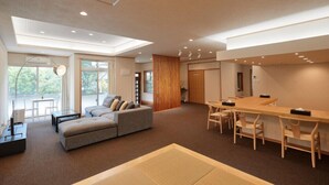 Una habitación de hotel moderna con sofá, mesa de comedor, sillas y ventanas amplias que ofrecen vistas al exterior.