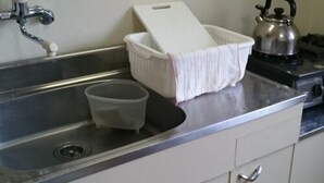 Une cuisine équipée d’un évier en acier inoxydable, d’une bouilloire et d’un récipient en plastique blanc.