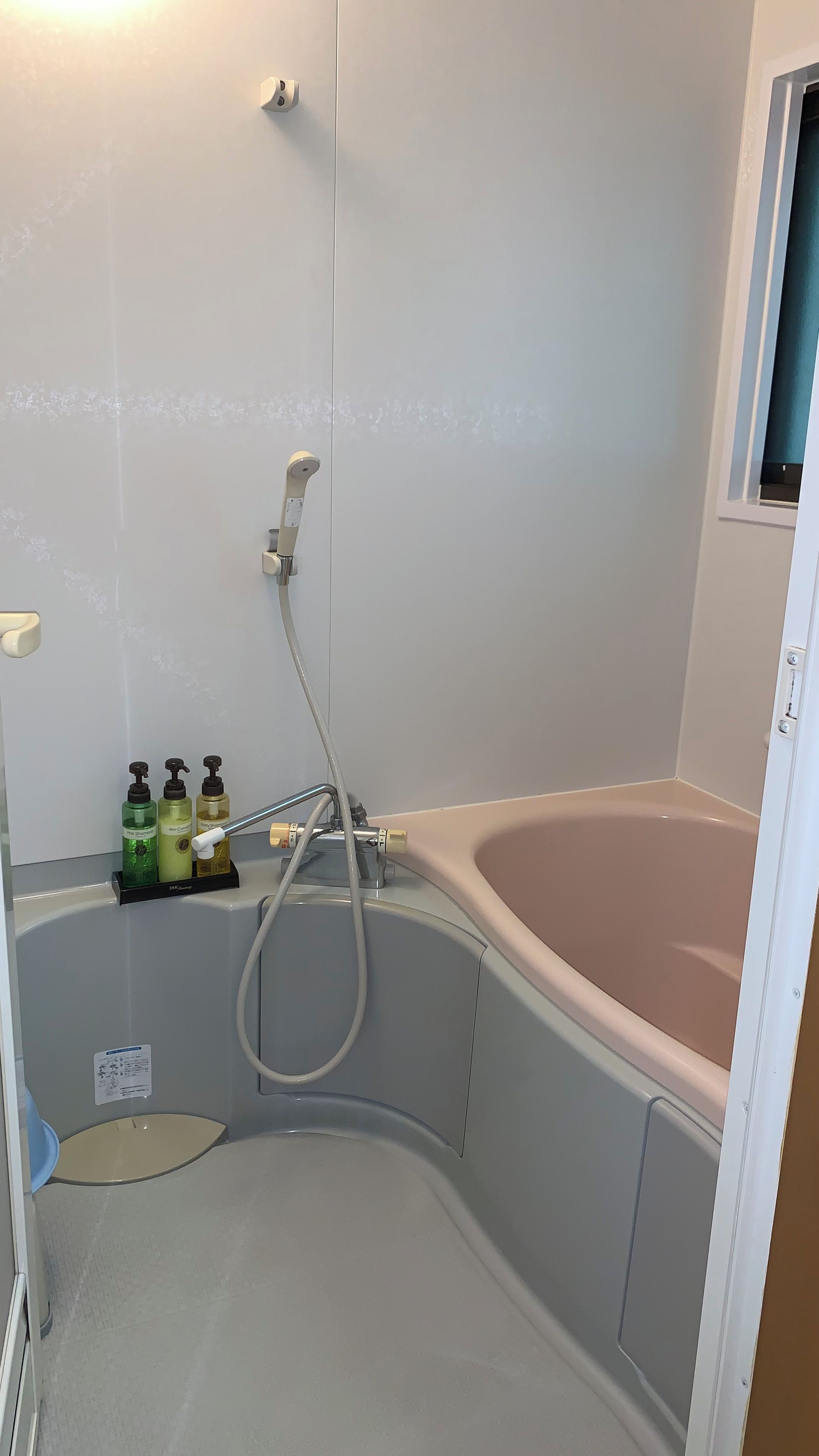 Een badkamer met een badkuip, douche en toilet. Drie flessen shampoo en conditioner staan op de muur.