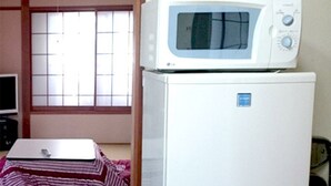Une pièce avec un réfrigérateur blanc, un four à micro-ondes posé sur le dessus, un téléviseur sur un meuble et une fenêtre avec des stores.