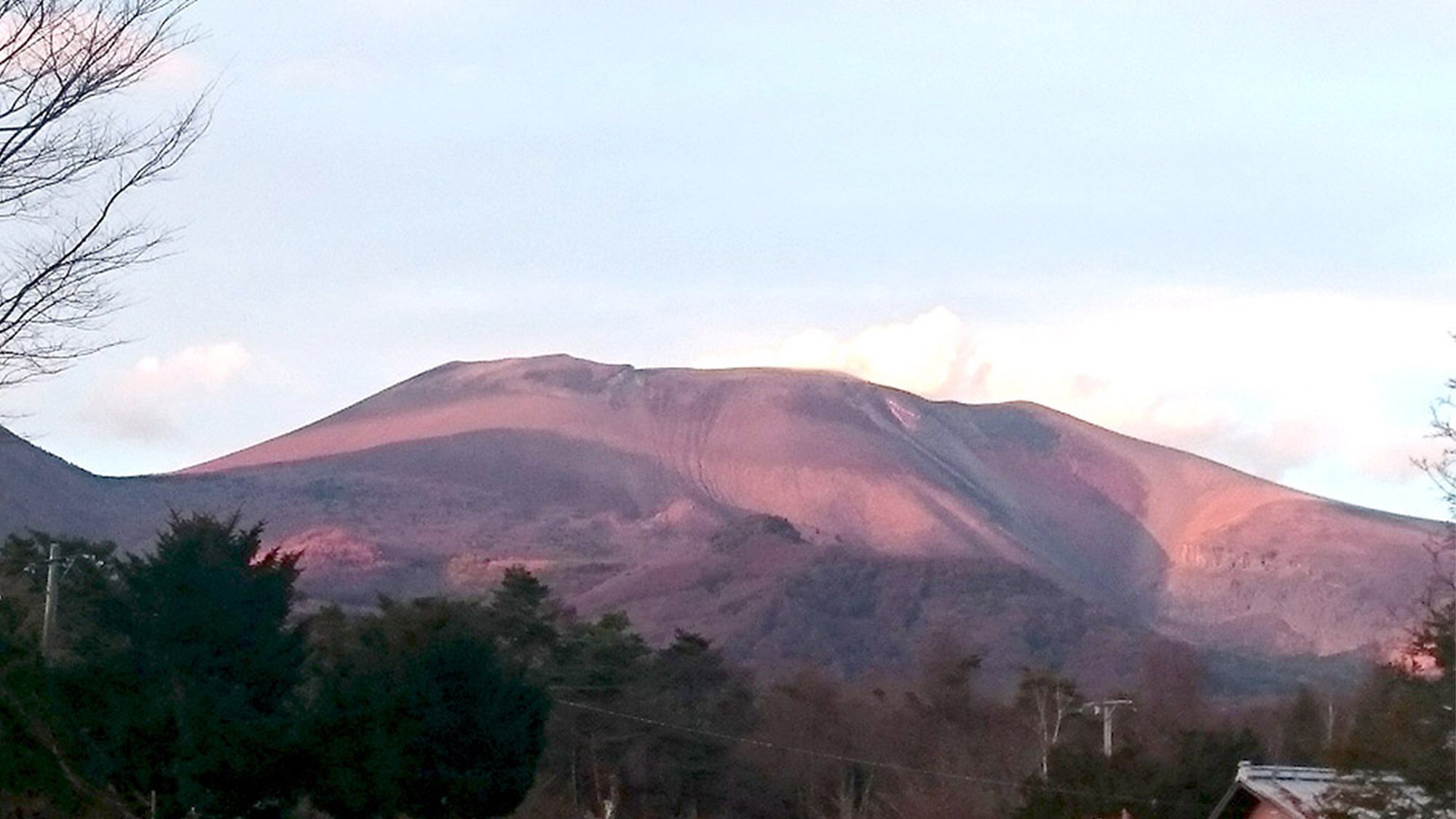 A mountain with a gentle slope and a flat summit, surrounded by trees and a few buildings.